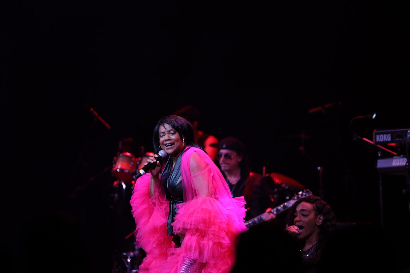 A woman in pink feathers singing into a microphone.