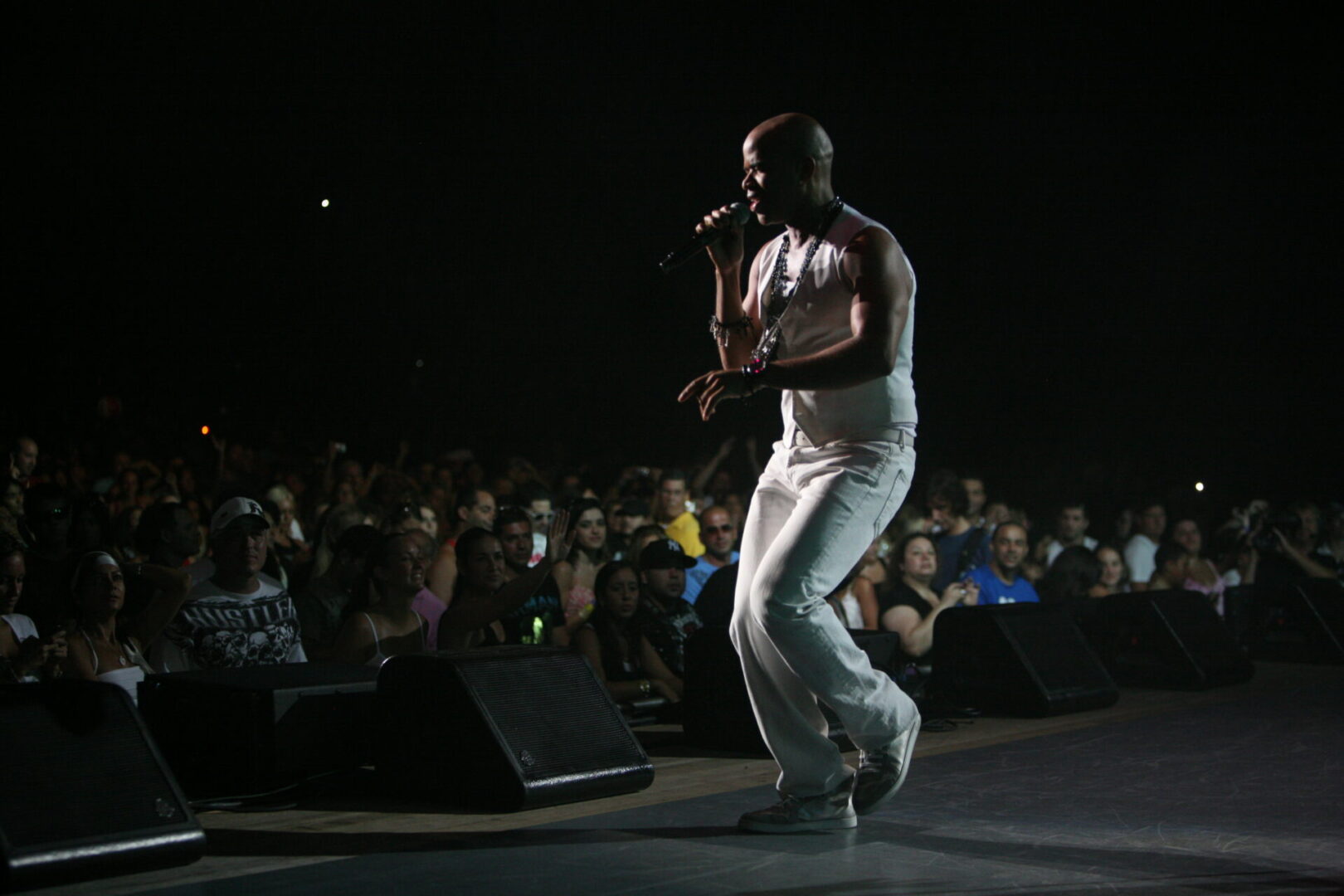 A man in white shirt and pants singing on stage.