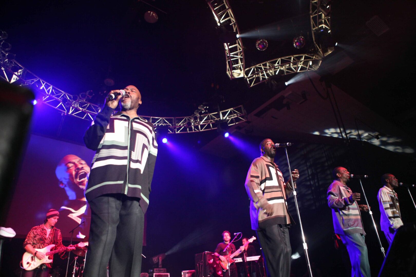 A group of men singing on stage with lights in the background.