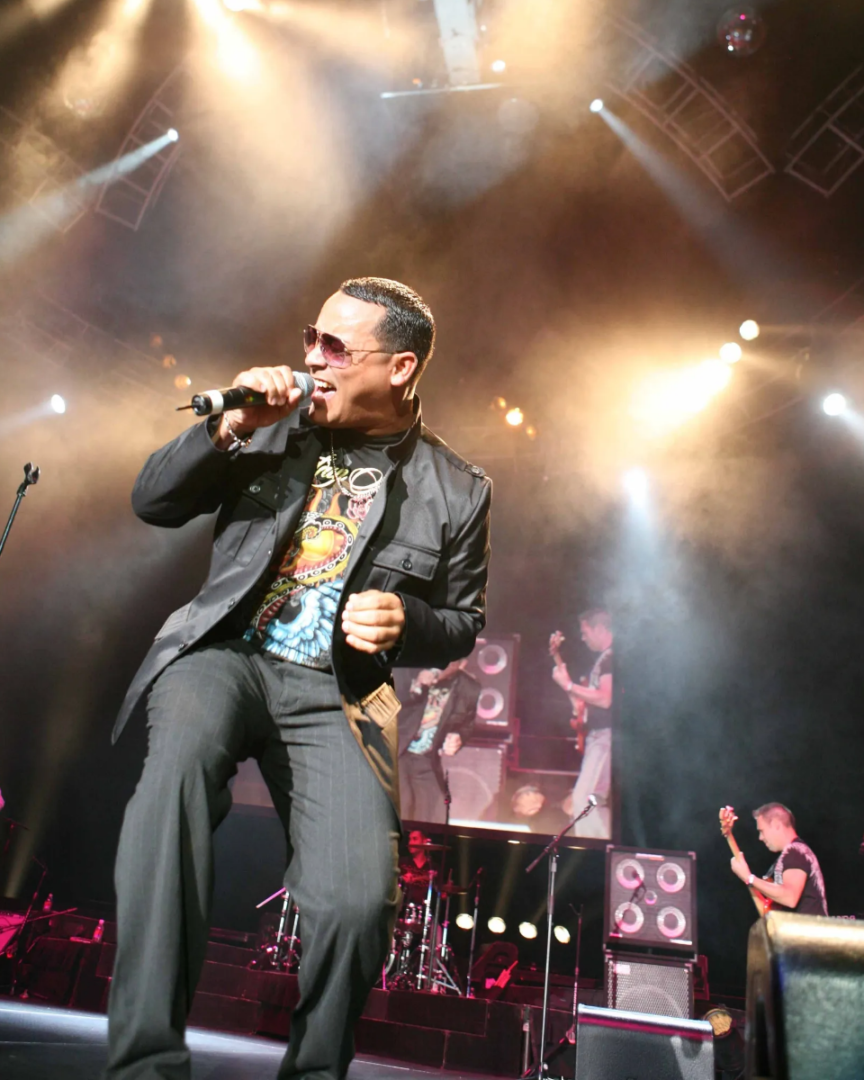 A man in black jacket and sunglasses singing on stage.